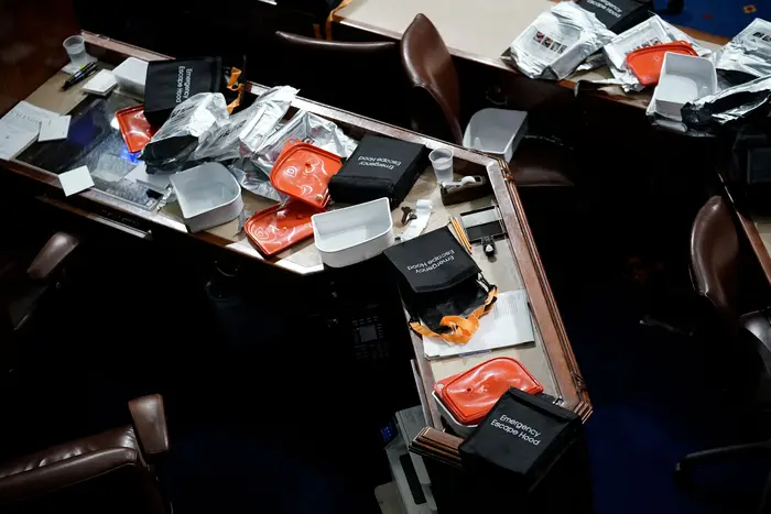An aerial photograph of the House chamber's desks, which has the empty Emergency Escape hood boxes